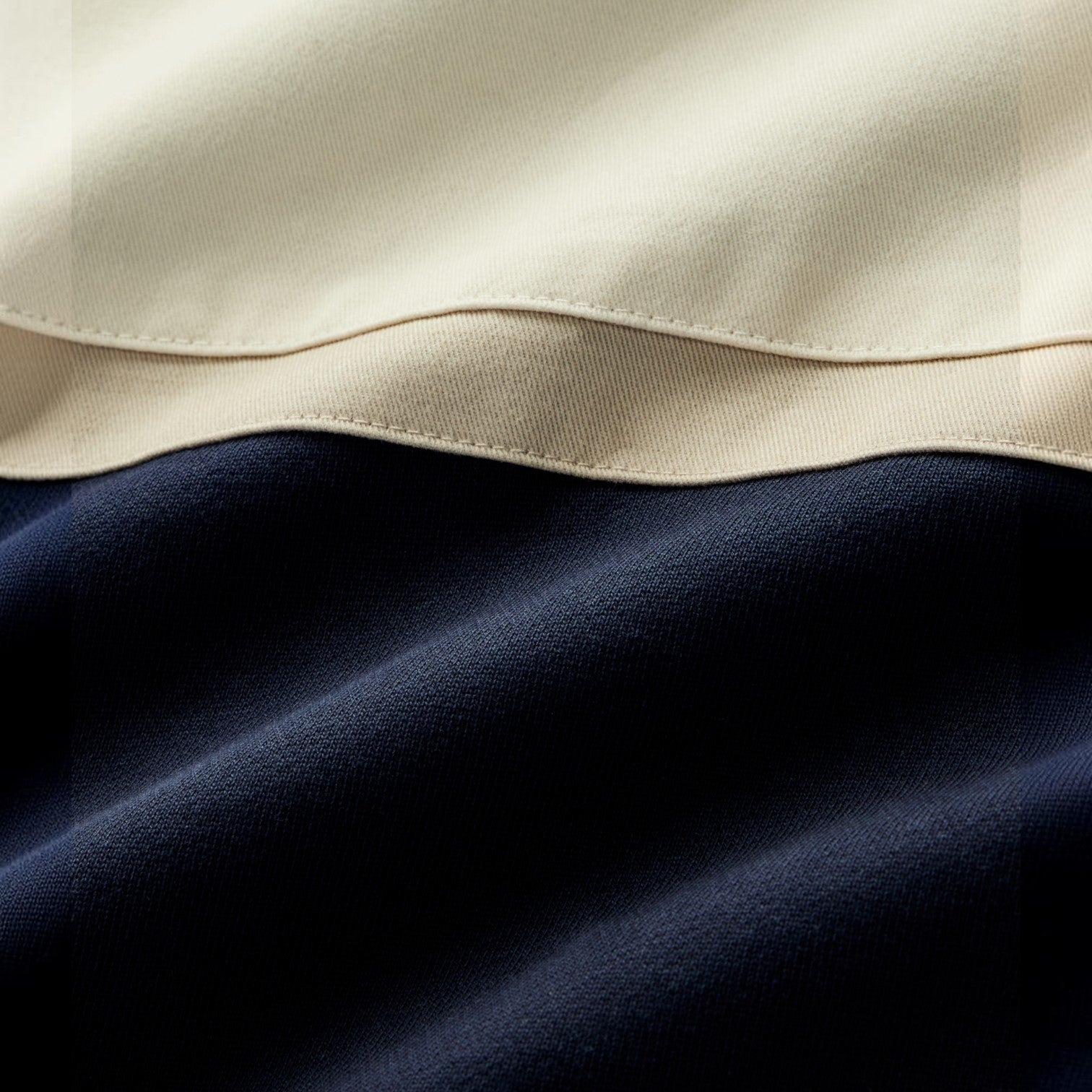 Close-up of a fabric product showing a two-tone color-block design with a cream upper section and a dark navy lower section, separated by a stitched seam.