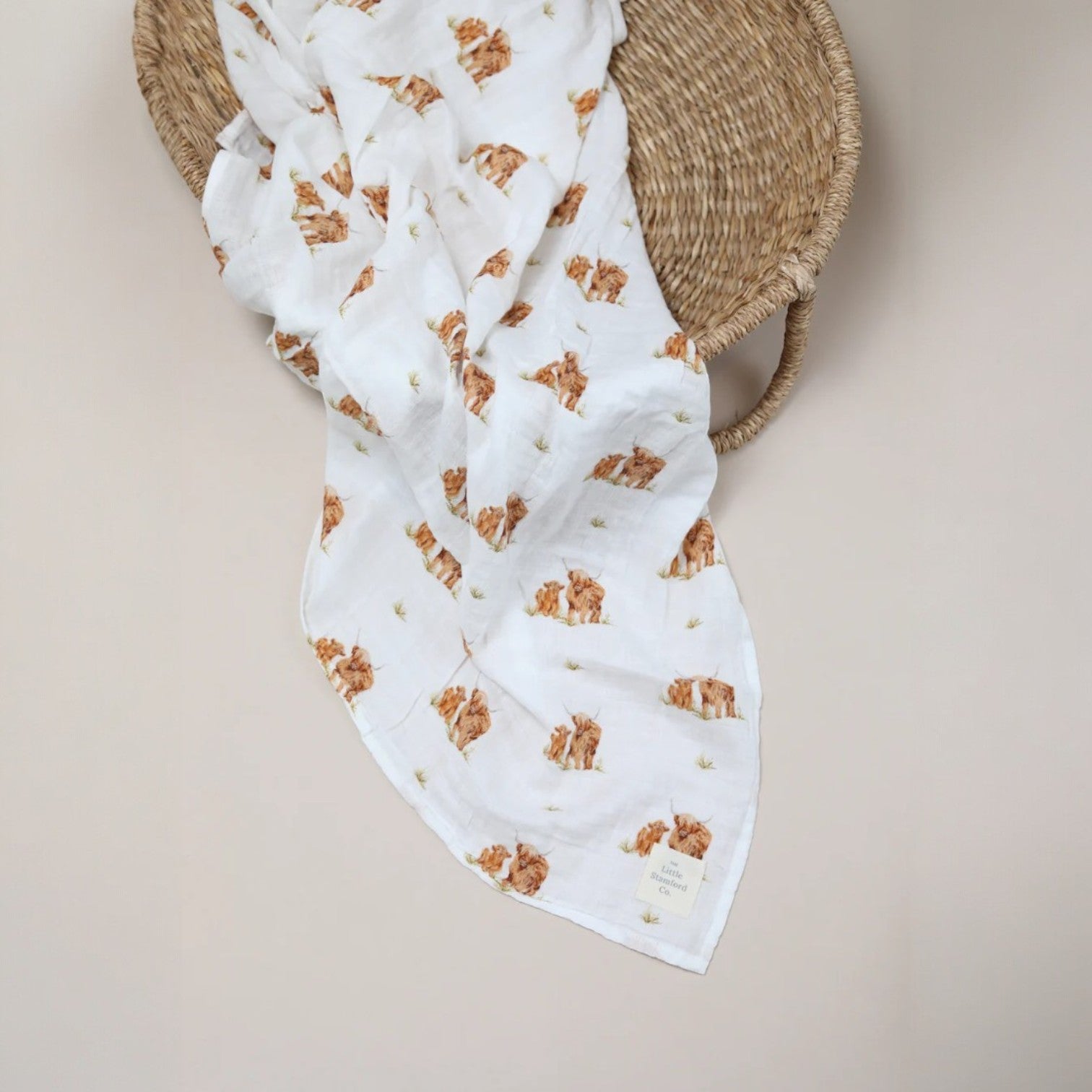 White baby blanket with brown bear pattern draped over a woven basket on a beige background