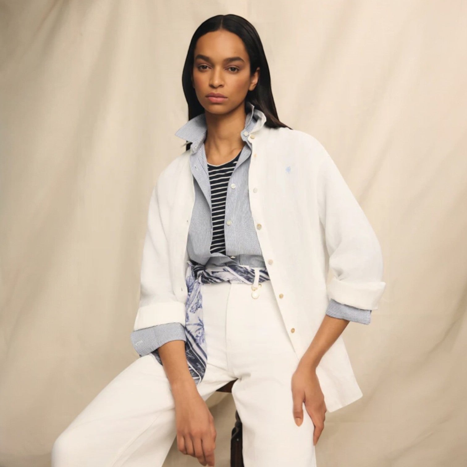 Woman wearing a white coat over a striped shirt on a beige background