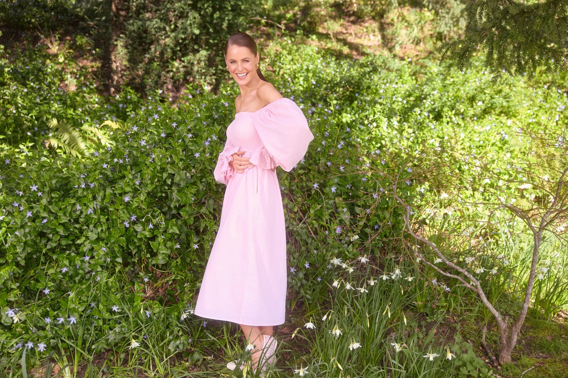 Woman in a pink dress standing in a garden with greenery and flowers.