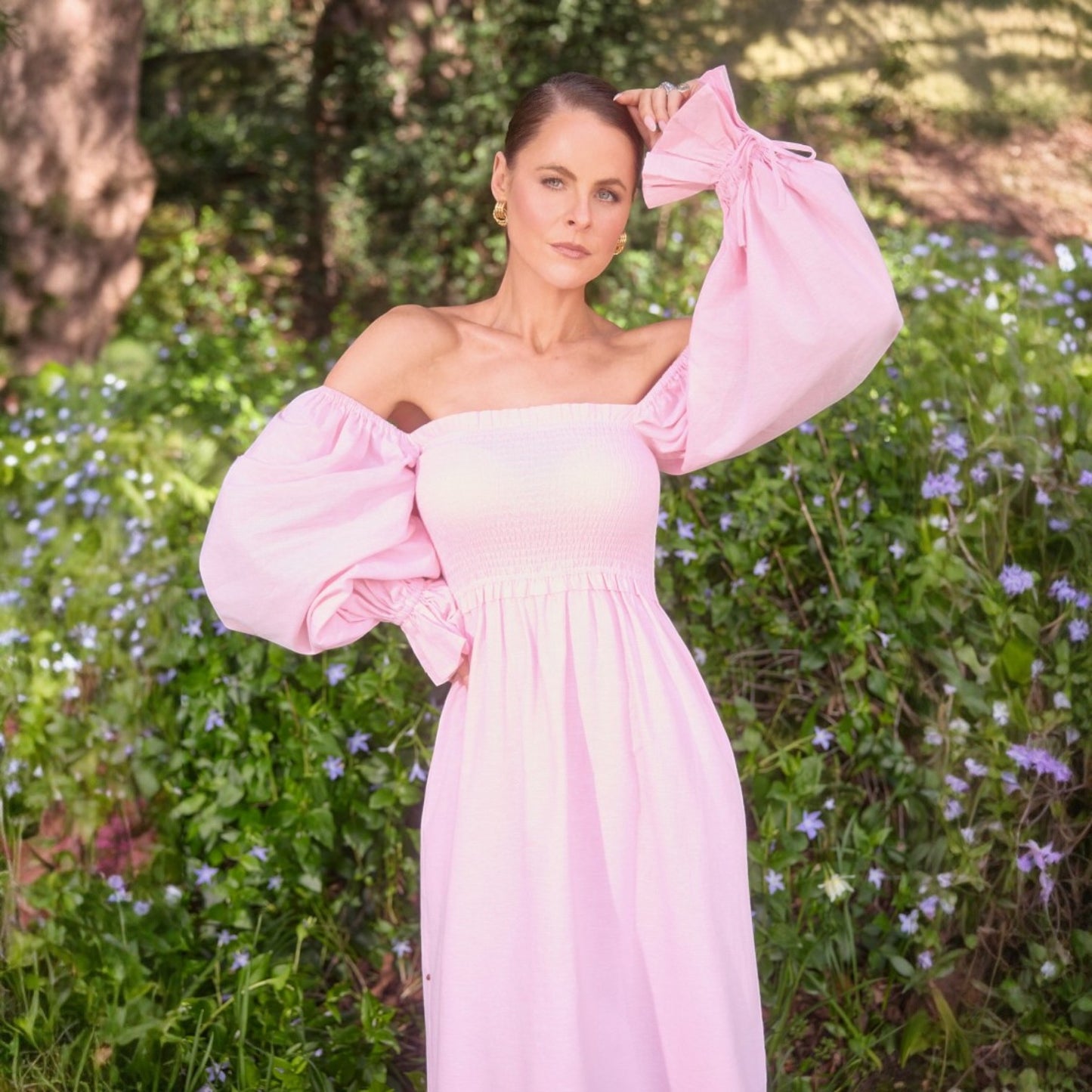 Woman in a pink dress standing in a garden with flowers and trees.