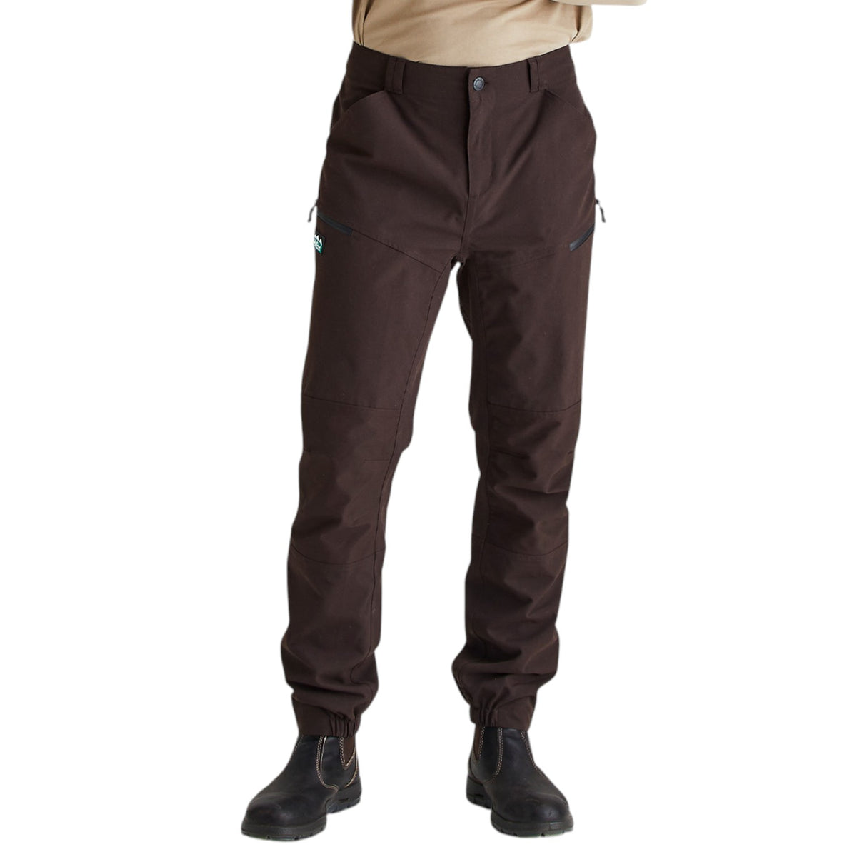 A person wearing dark brown technical pants with zippered pockets and elastic cuffs, paired with black boots against a plain white background.