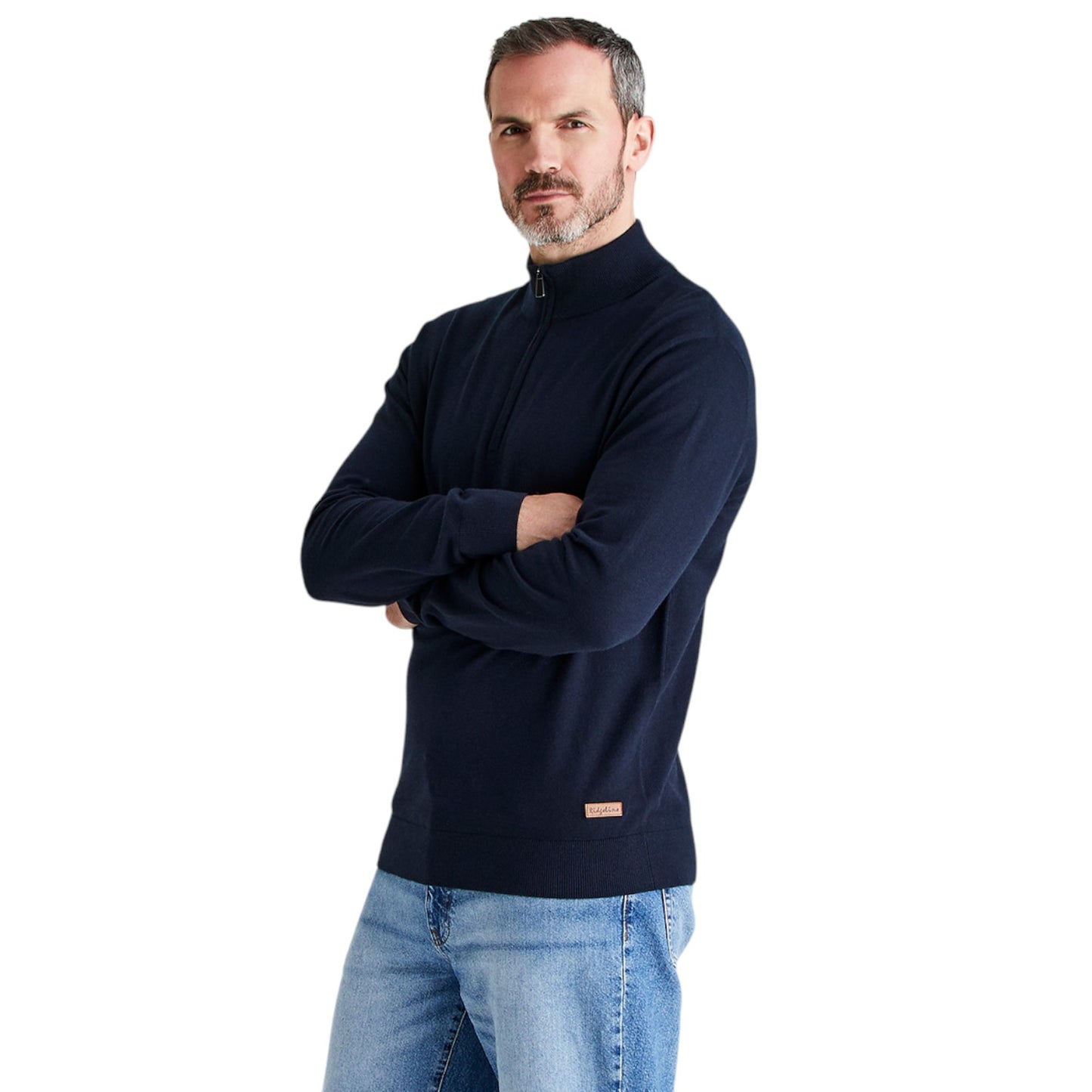 A man wearing a dark navy blue quarter-zip mock-neck sweater and light blue jeans, standing with arms crossed against a solid white background.