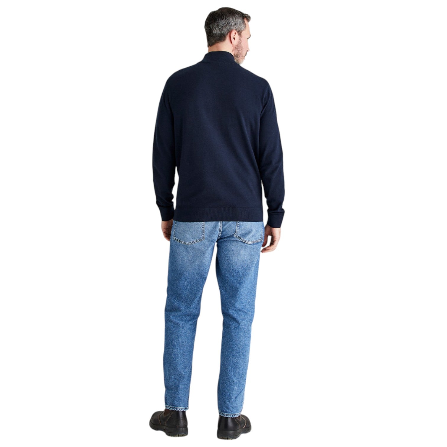 A man viewed from the back wearing a dark navy long-sleeve knit sweater and blue jeans, standing against a plain white background.