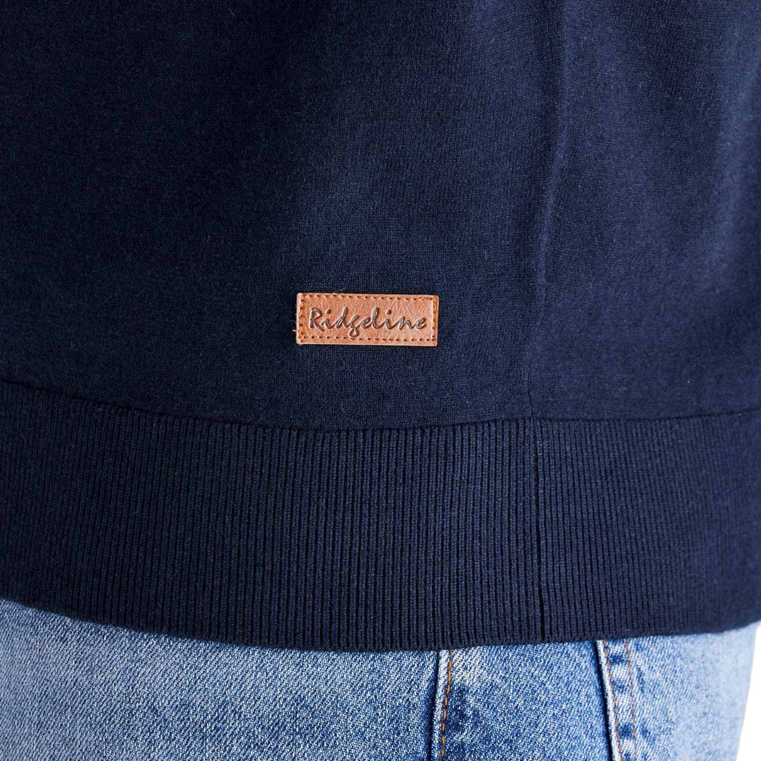 Close-up of a navy blue ribbed knit top with a small brown leather patch on the chest reading 'Ridgeline', worn with light blue jeans.