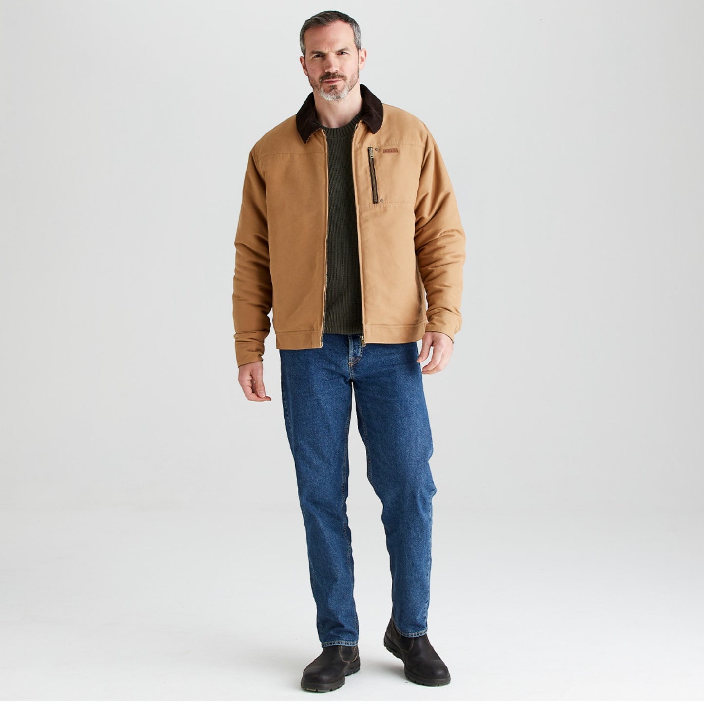 Man wearing a tan jacket and blue jeans on a white background
