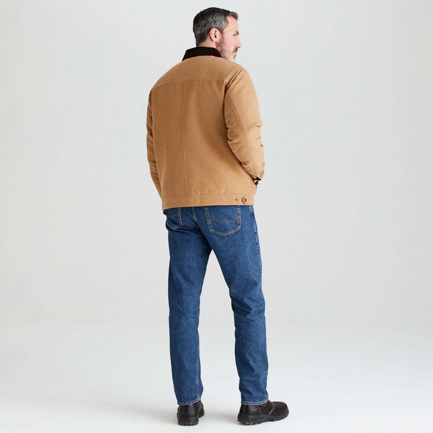 Man wearing a brown jacket and blue jeans on a light gray background