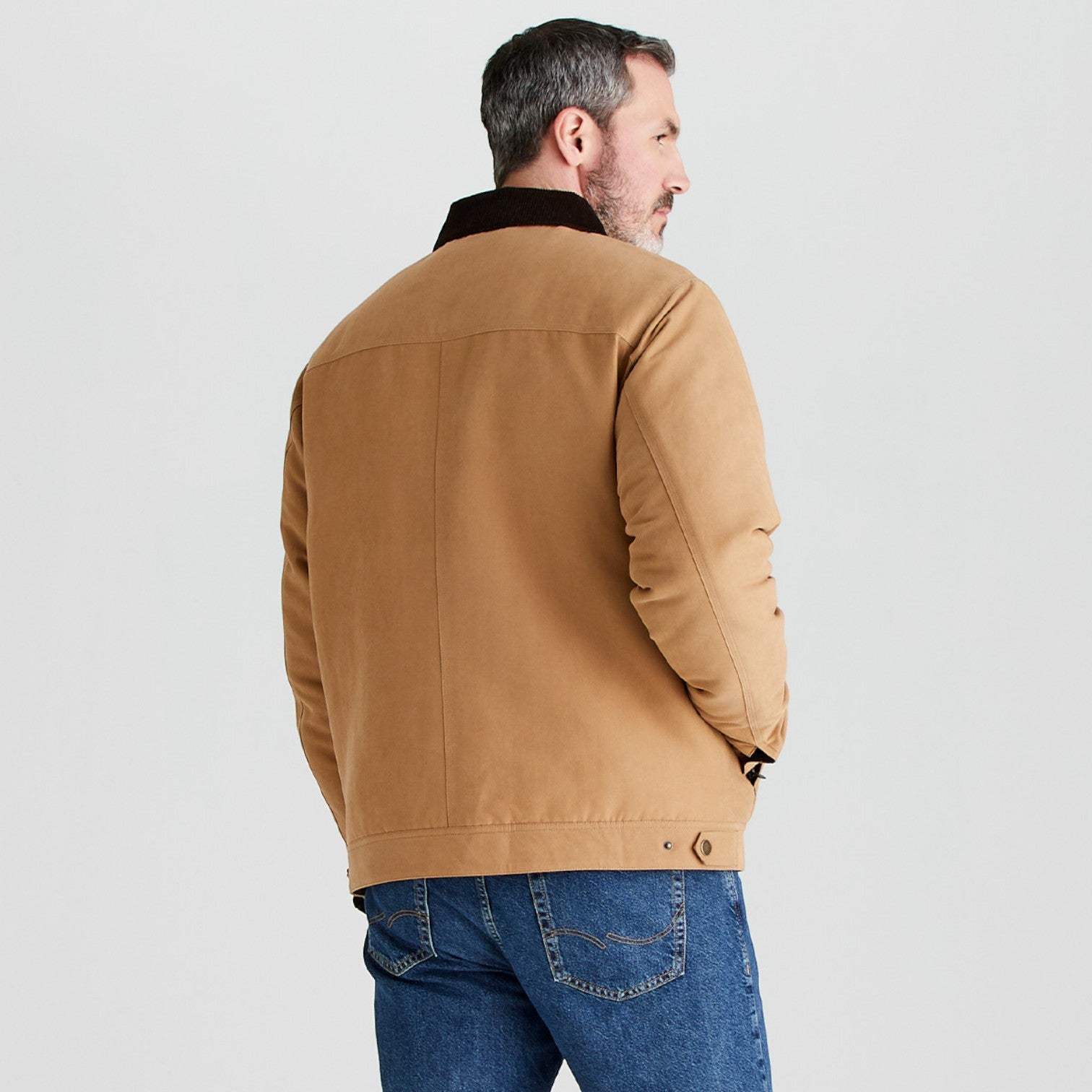 Man wearing a brown jacket and blue jeans on a light gray background