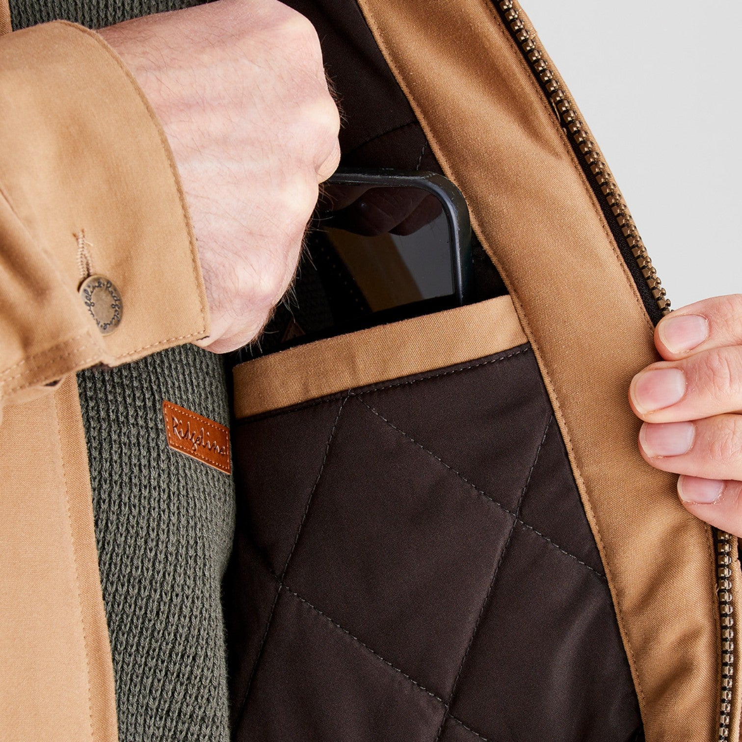 Close-up of a person wearing a tan jacket with a quilted black lining, holding a smartphone.