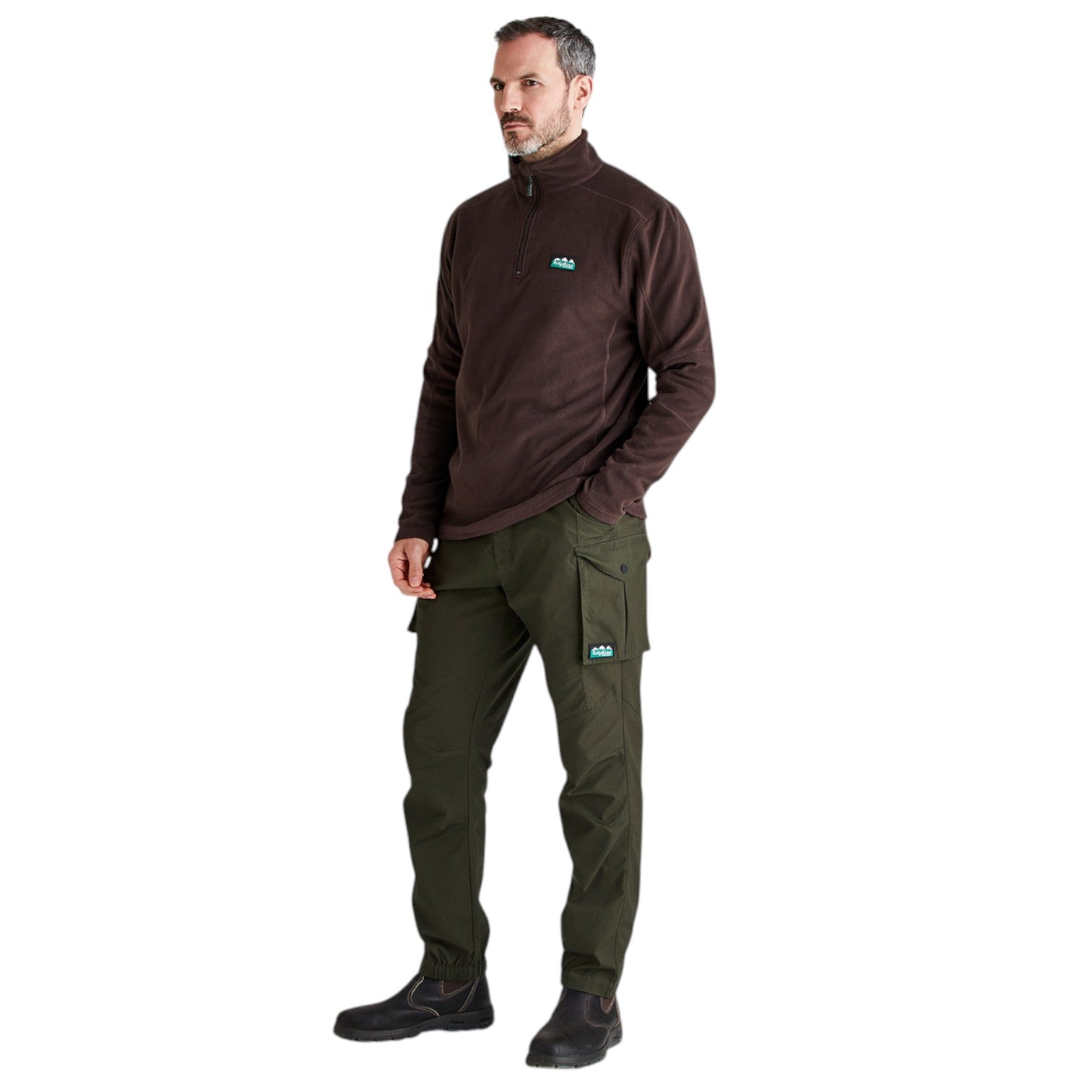 A man modeling a dark brown quarter-zip fleece pullover and olive green cargo pants with small turquoise ALO logos on the chest and thigh, set against a plain white background.