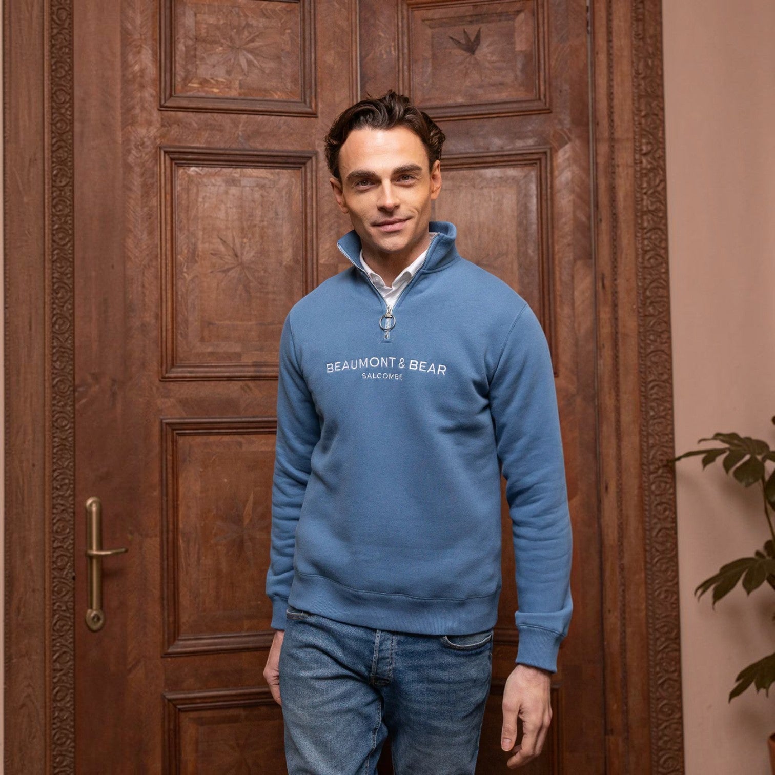 Man wearing a blue Beaumont & Bear sweatshirt standing in front of a wooden door.
