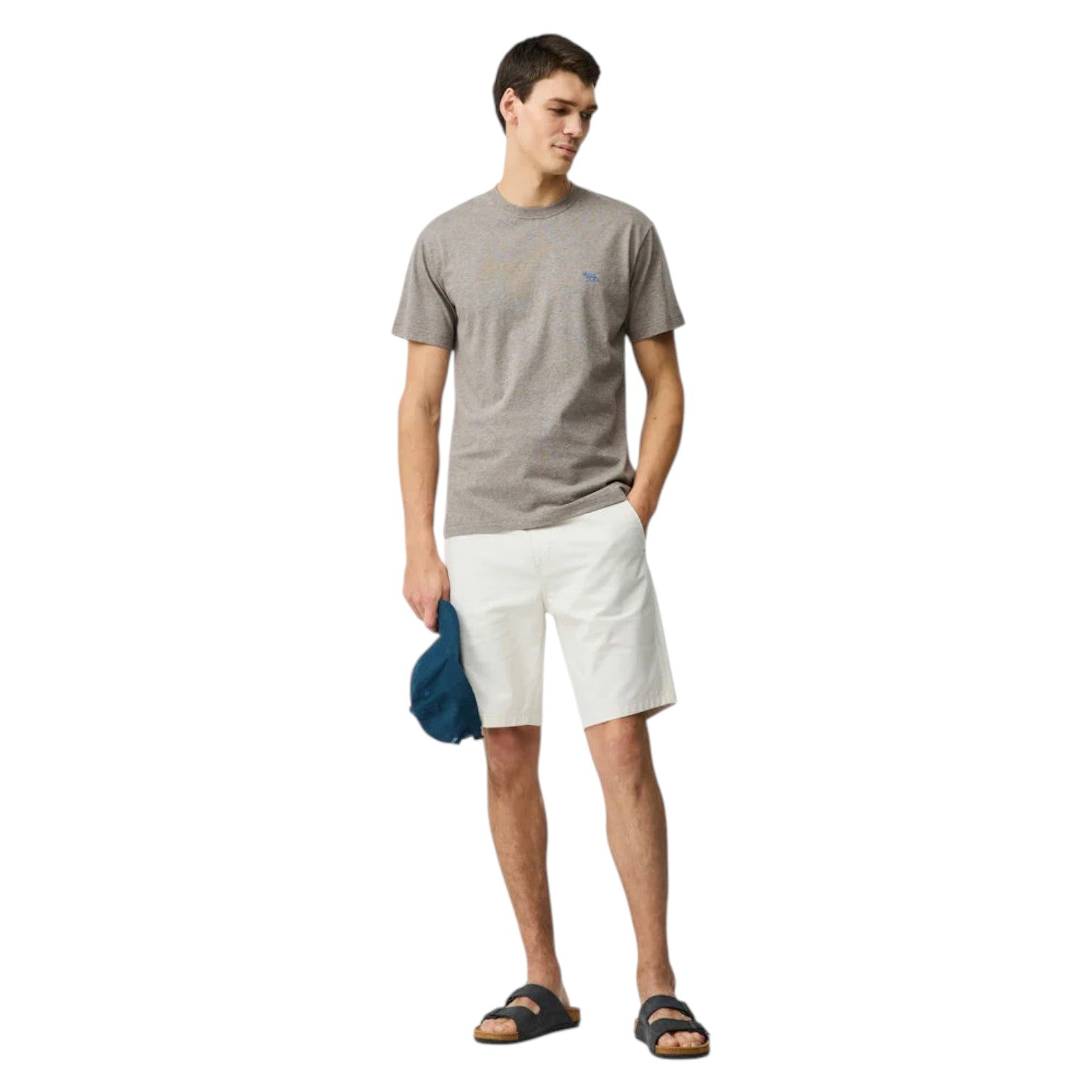 Man wearing a gray t-shirt and white shorts holding a blue cap on a white background