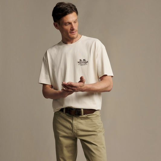 A man wearing a cream-colored short-sleeve t-shirt with a black 'B.M.