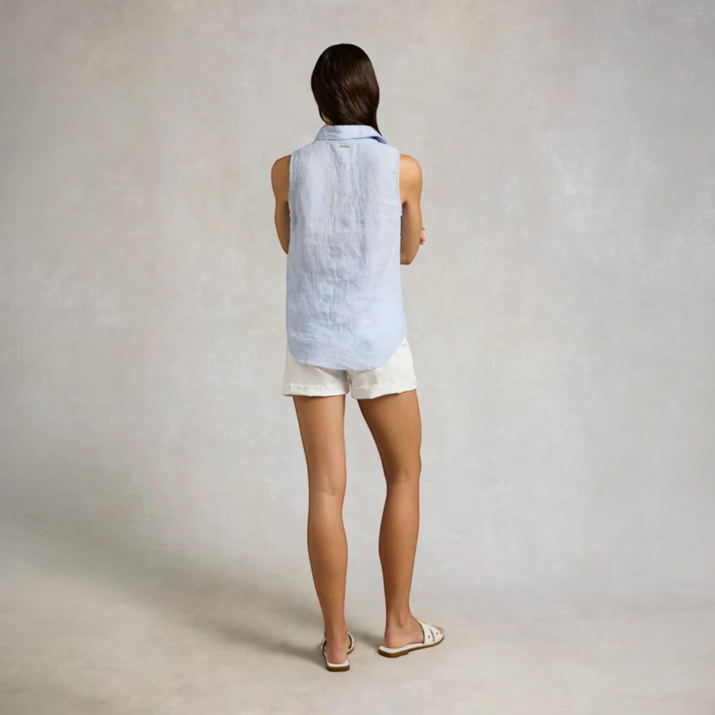 Person wearing a light blue sleeveless top and white shorts on a plain background