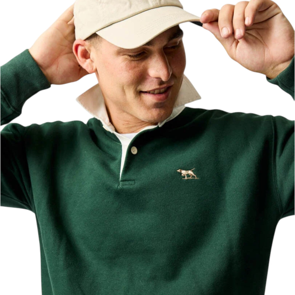 Man wearing a green polo shirt with a logo, adjusting a beige cap on a white background