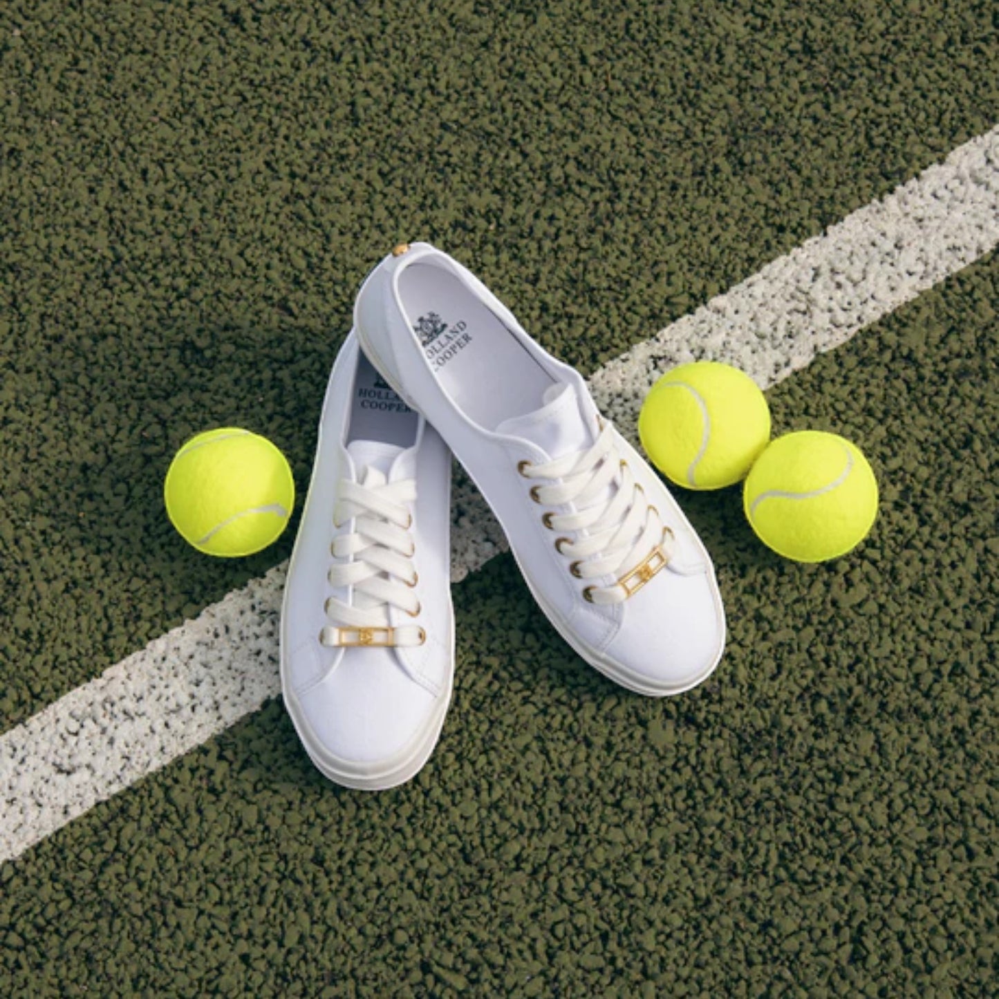 White sneakers with gold accents on a tennis court with yellow tennis balls.