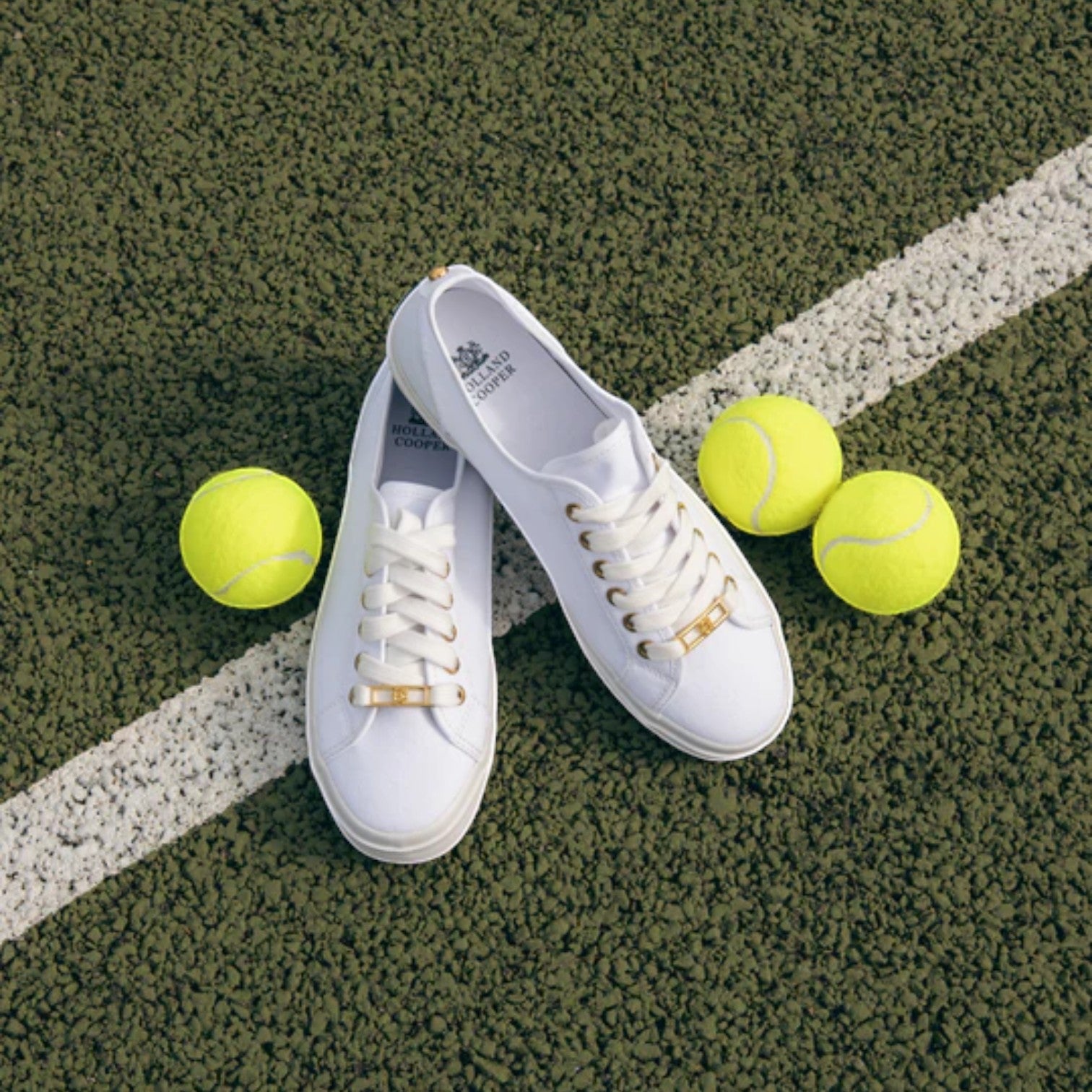 White sneakers with gold accents on a tennis court with yellow tennis balls.
