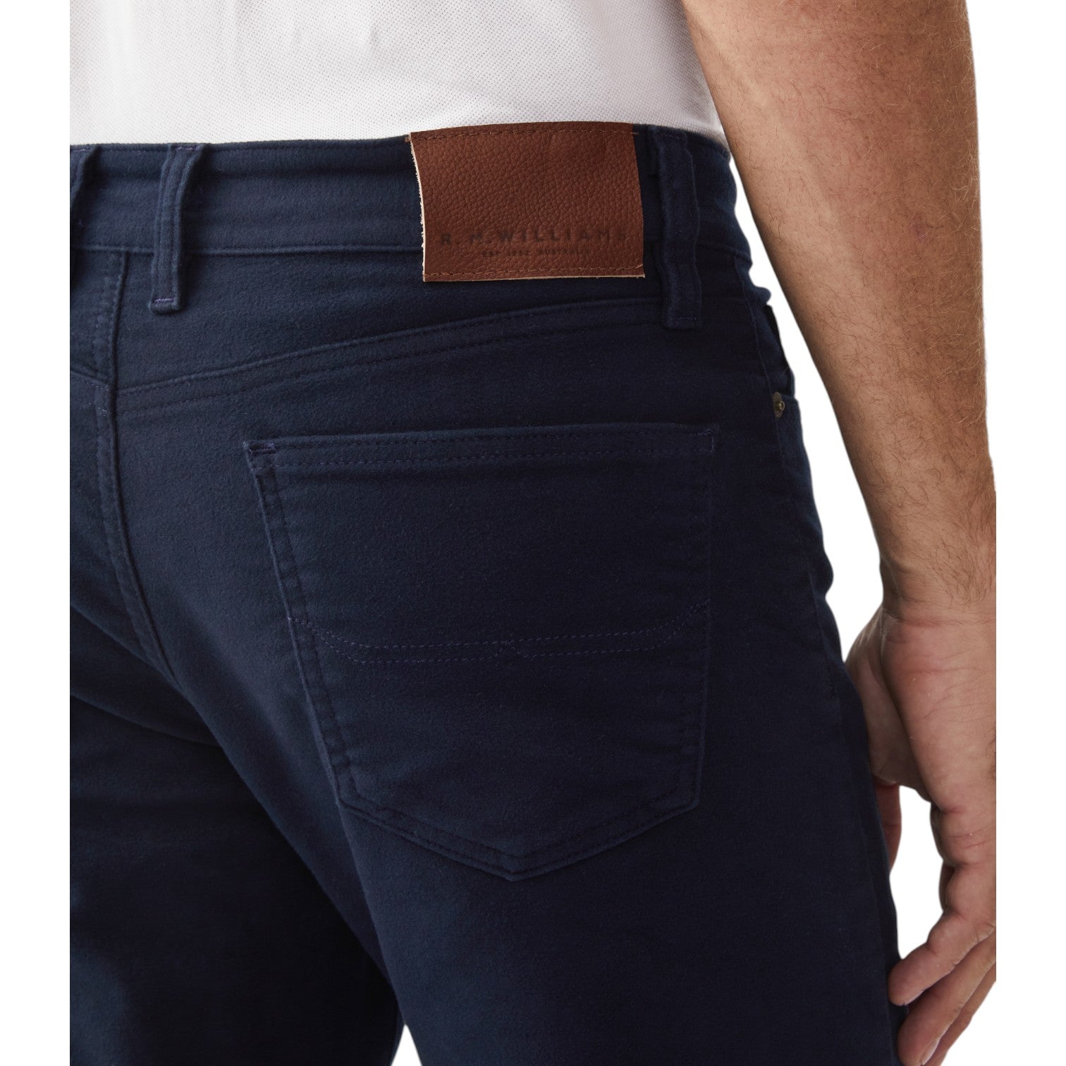 Navy blue jeans with a brown patch on the back pocket against a white background