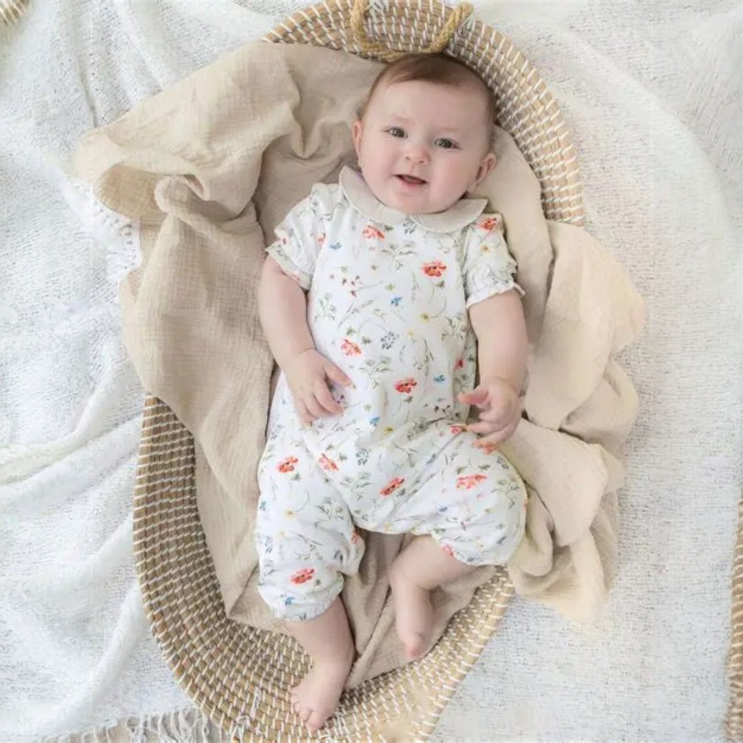 Baby in a floral onesie sitting in a woven basket with a beige blanket