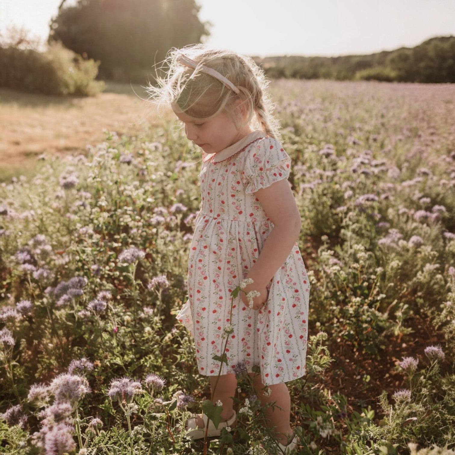 Young girl in a floral dress standing in a field of flowers.