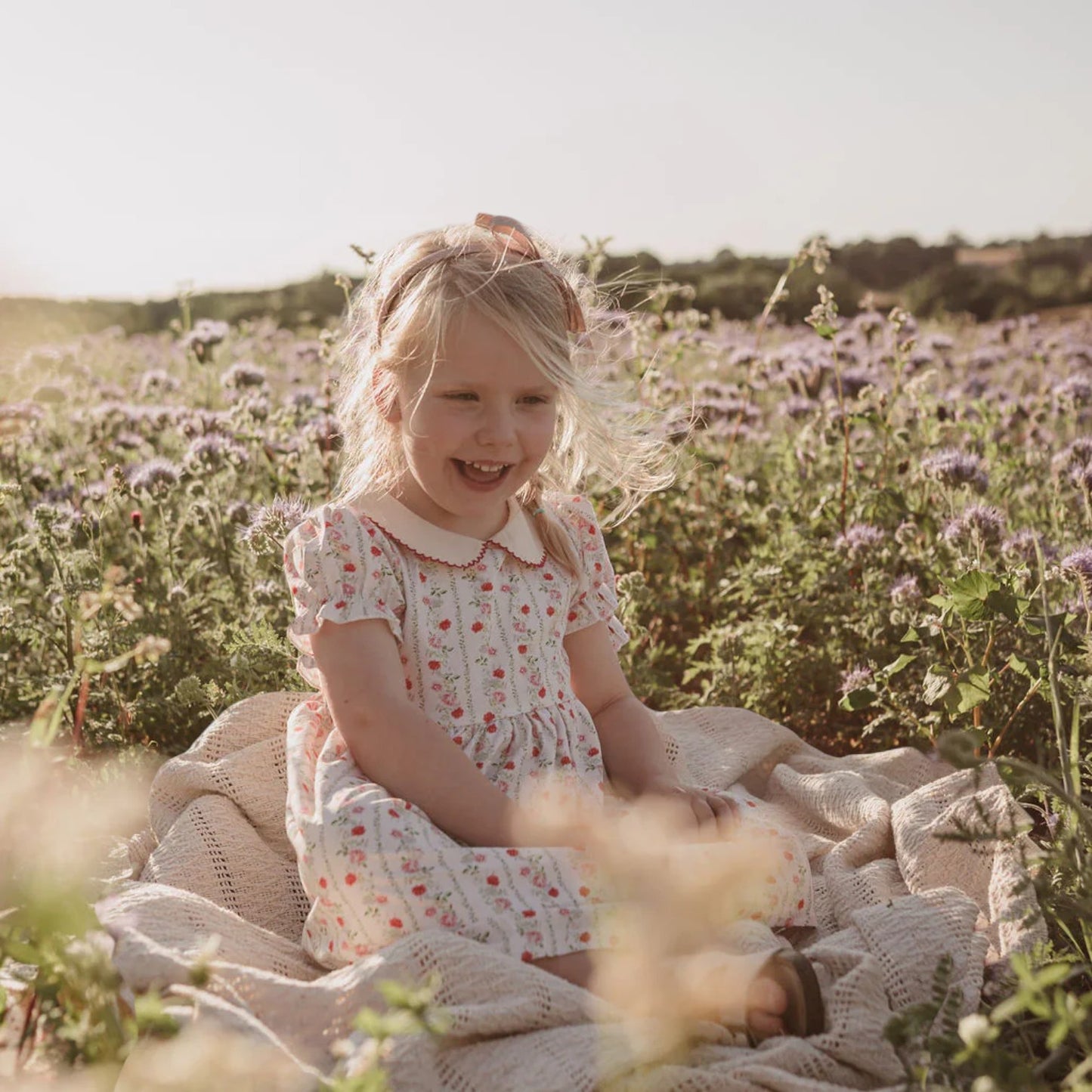 Young girl in a floral dress sitting on a blanket in a field of flowers.