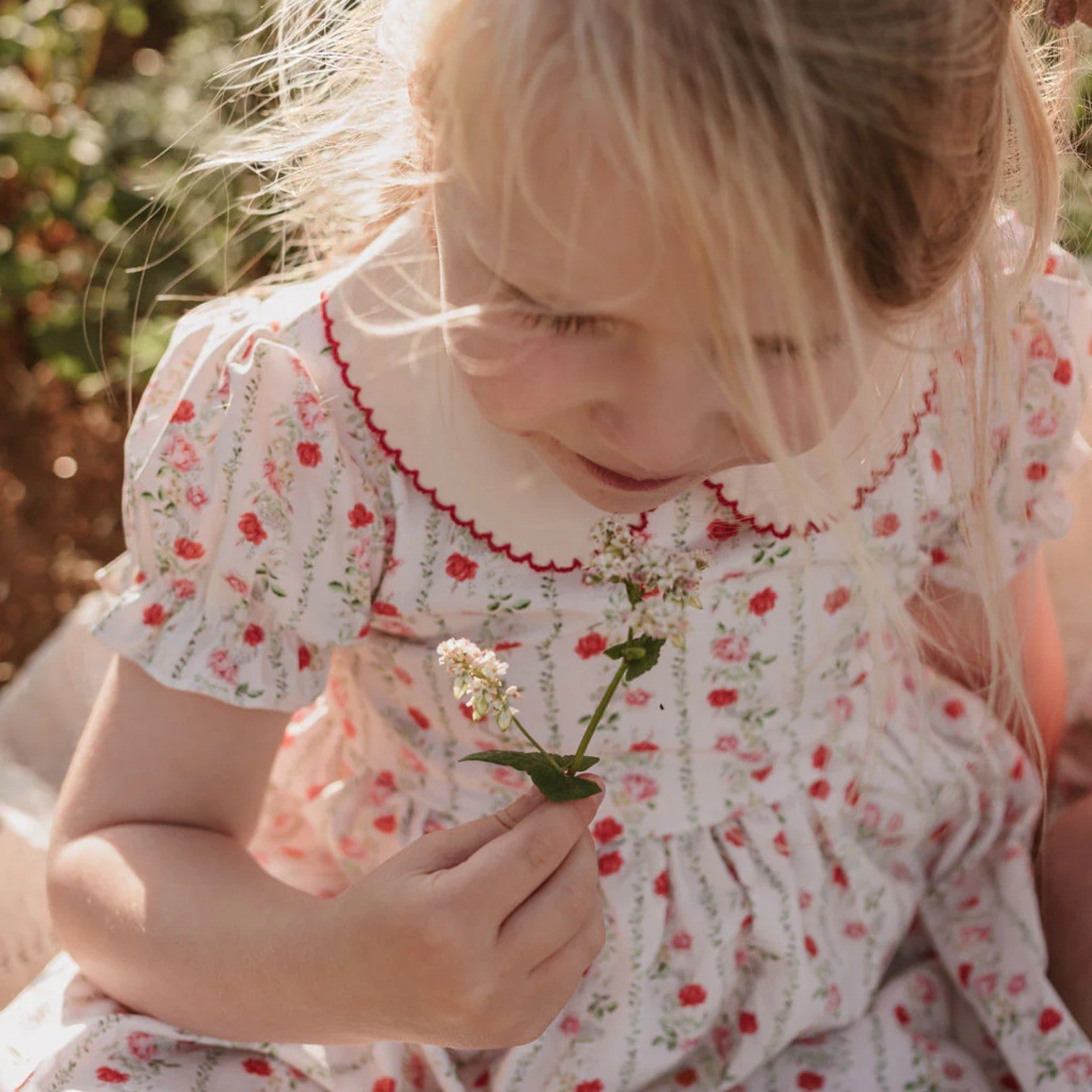 Young girl in a floral dress holding a flower outdoors