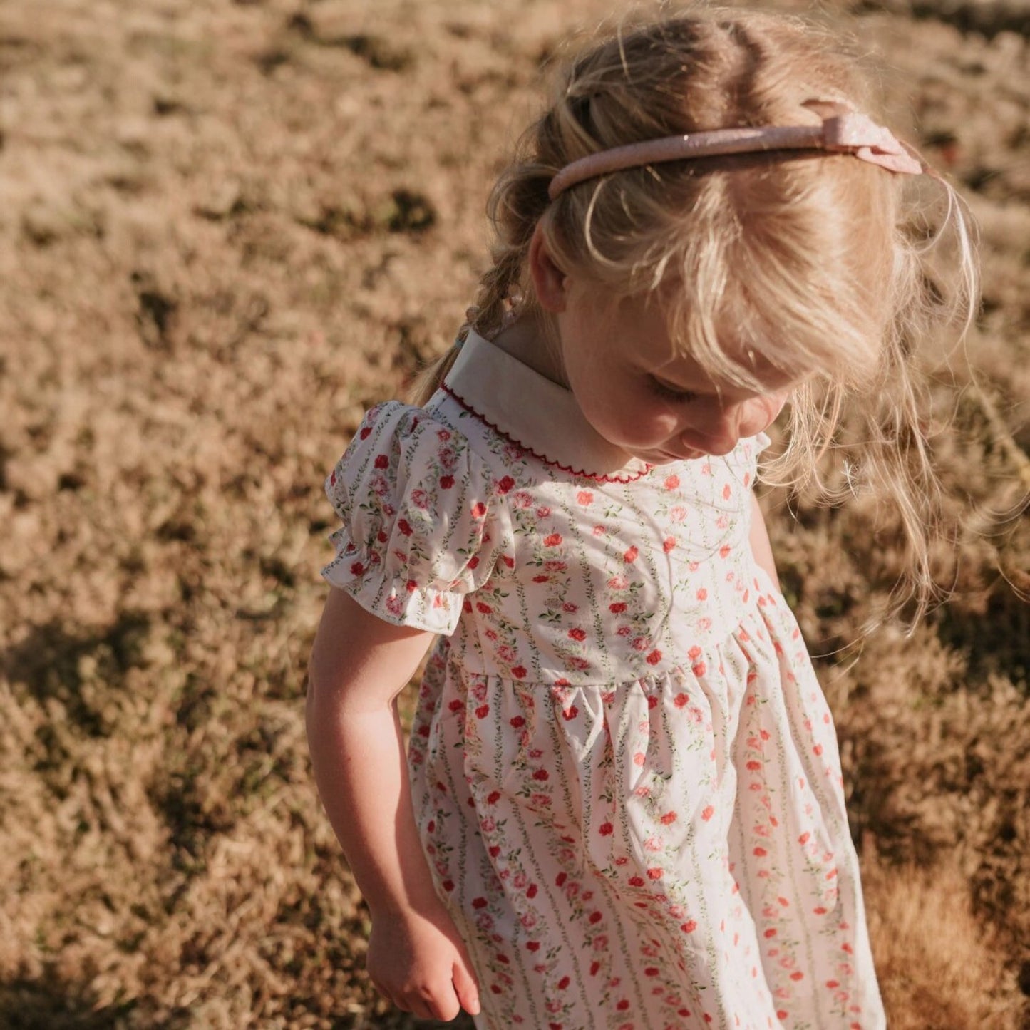 Young girl in a floral dress standing in a field with a blurred background