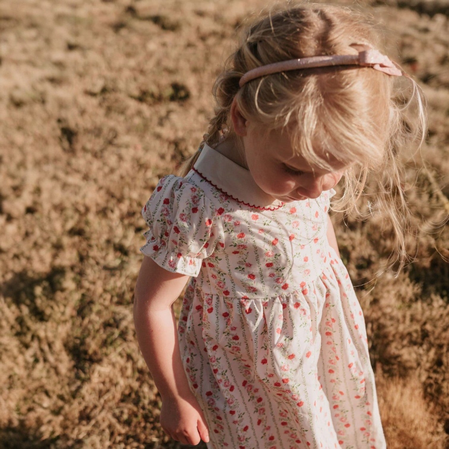 Young girl in a floral dress standing in a field with a blurred background