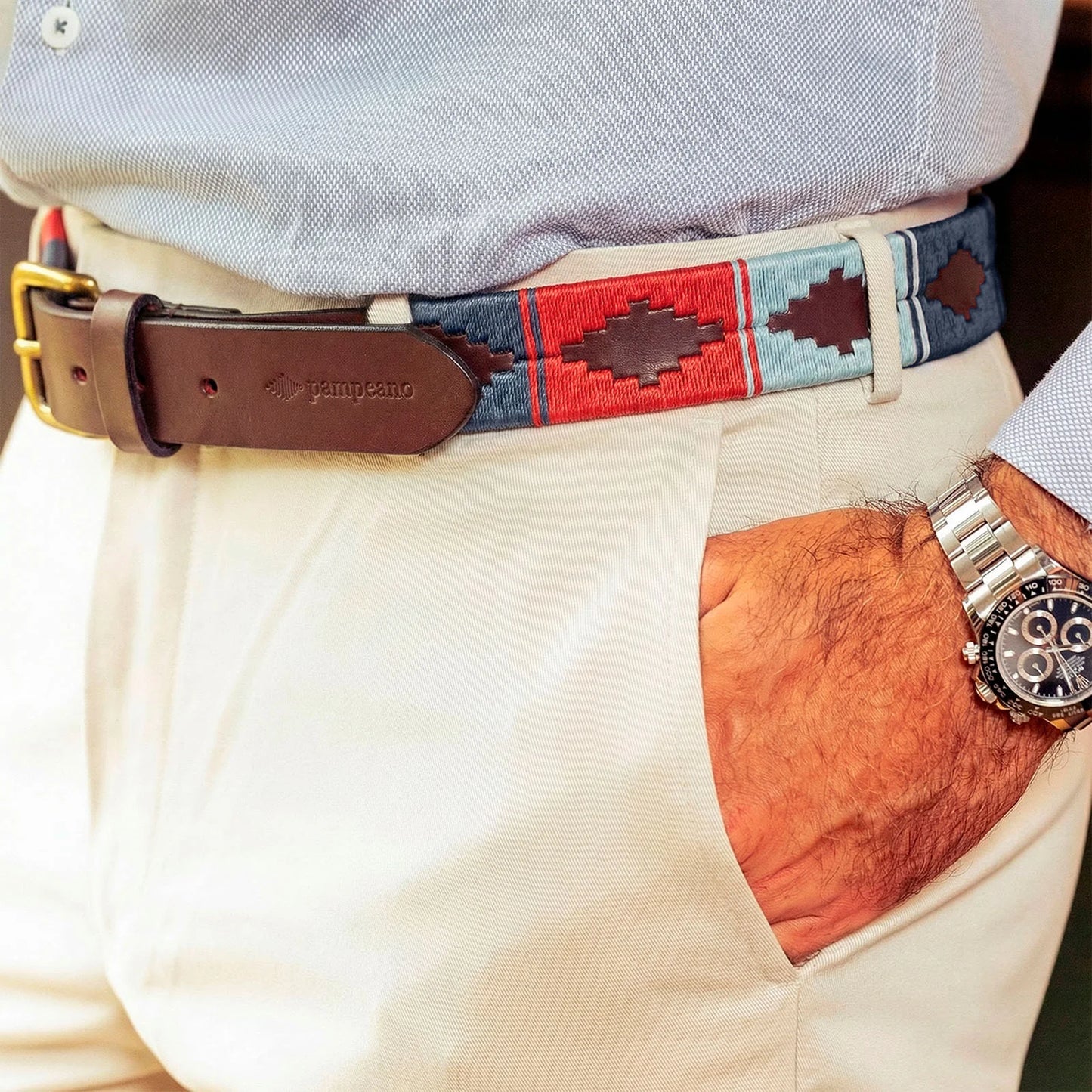 Person wearing a colorful belt with a brand logo, beige pants, and a watch.