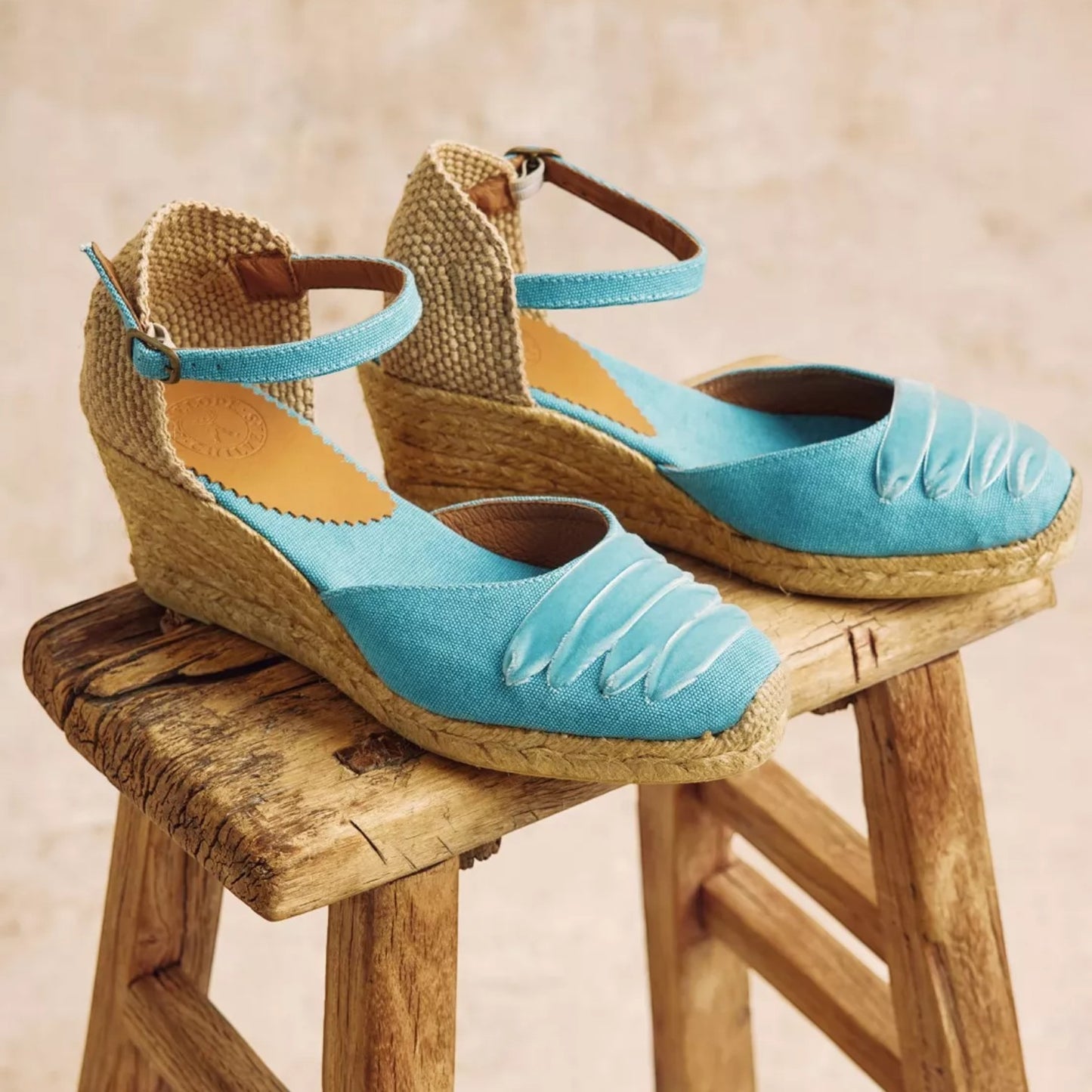 Pair of blue wedge sandals on a wooden stool with a beige background