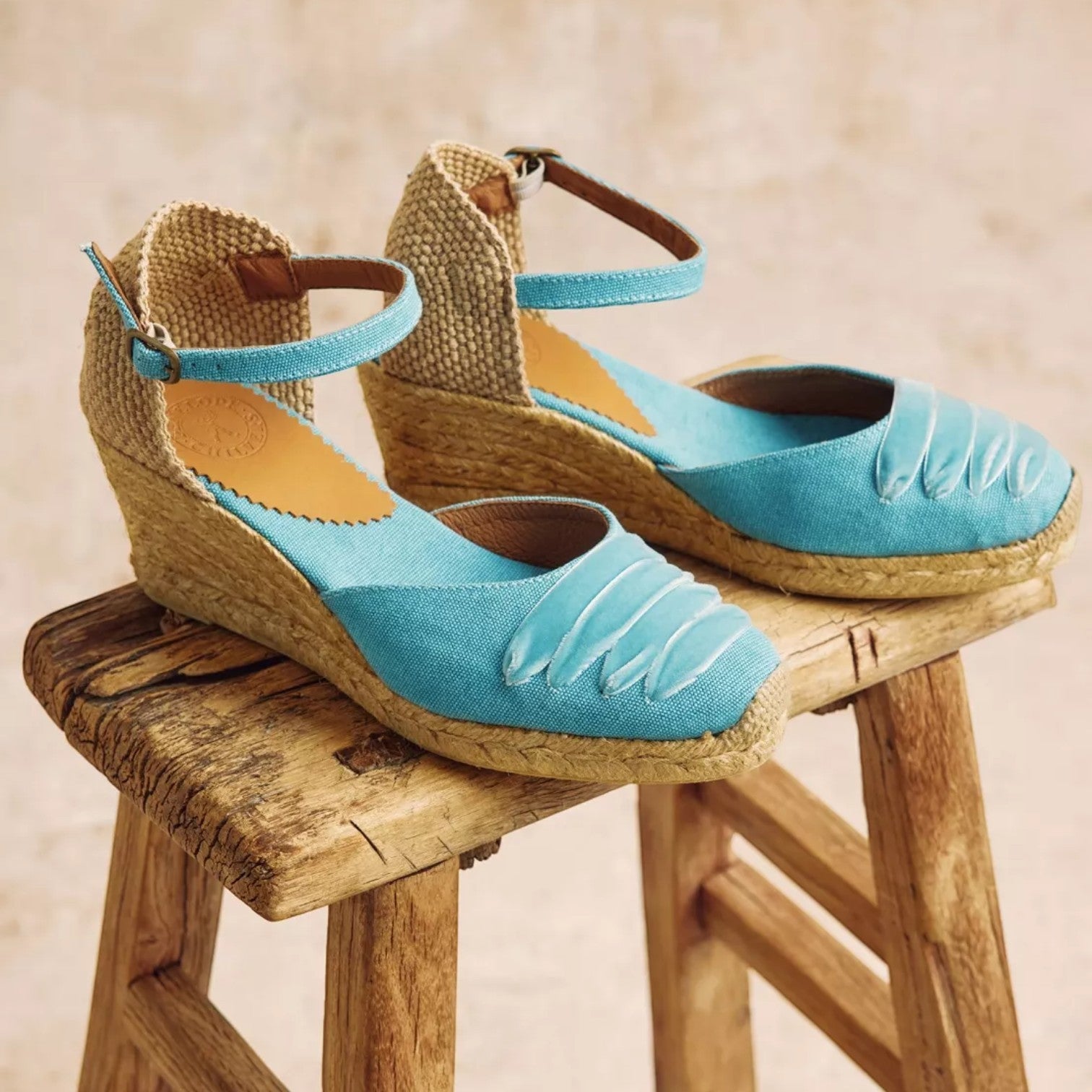 Pair of blue wedge sandals on a wooden stool with a beige background