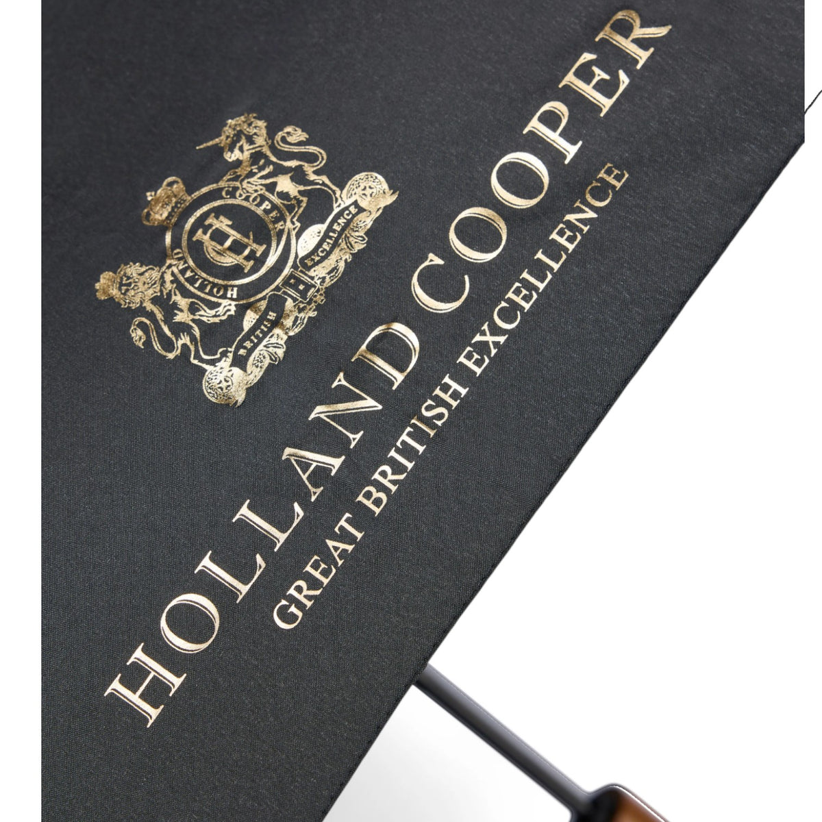 Close-up of a black umbrella canopy with gold foil embossed branding, including the Holland Cooper crest and the words 'HOLLAND COOPER' and 'GREAT BRITISH EXCELLENCE', shown against a white background.