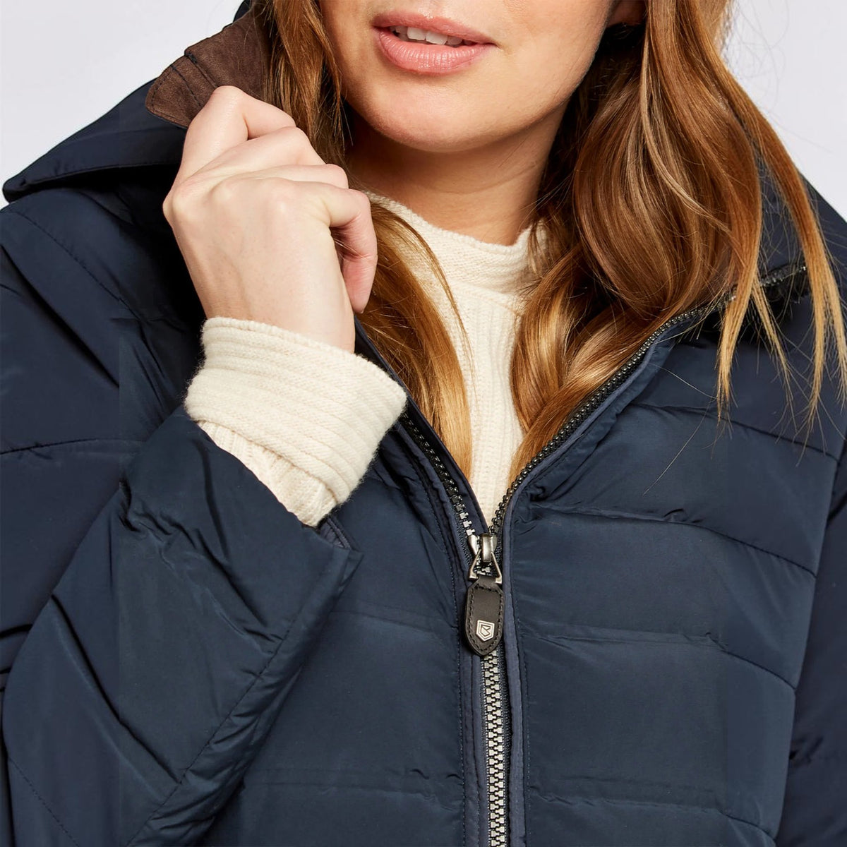 Close-up of a woman wearing a navy blue puffer jacket over a cream ribbed sweater, with her hand near the collar and zipper.