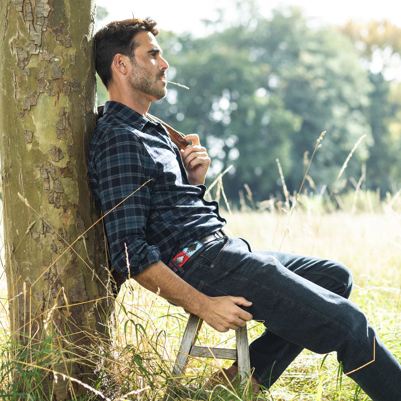 Man leaning against a tree in a field with a blurred natural background
