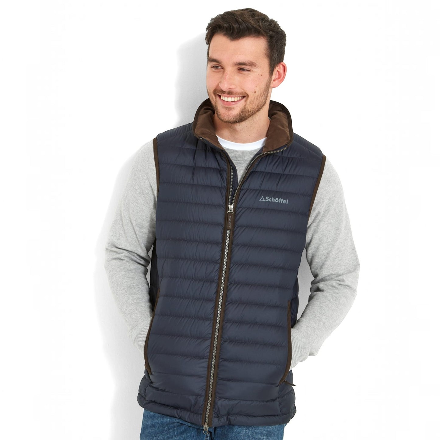 A man wearing a dark navy blue puffer vest with brown trim and a brown collar, layered over a light gray long-sleeve shirt. The brand name 'Menden' is visible on the chest.