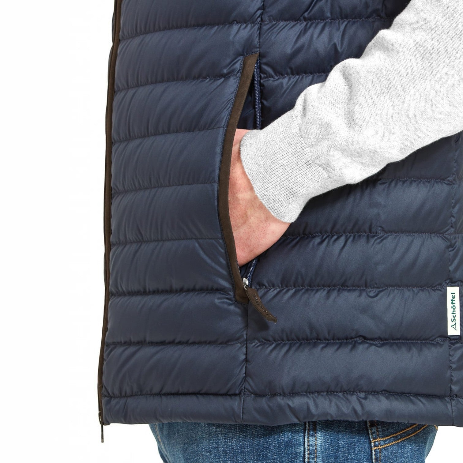 Close-up of a navy blue puffer vest with a side zipper pocket, shown on a model wearing a light gray sweater and blue jeans. The brand tag 'Scalpers' is visible on the lower right.