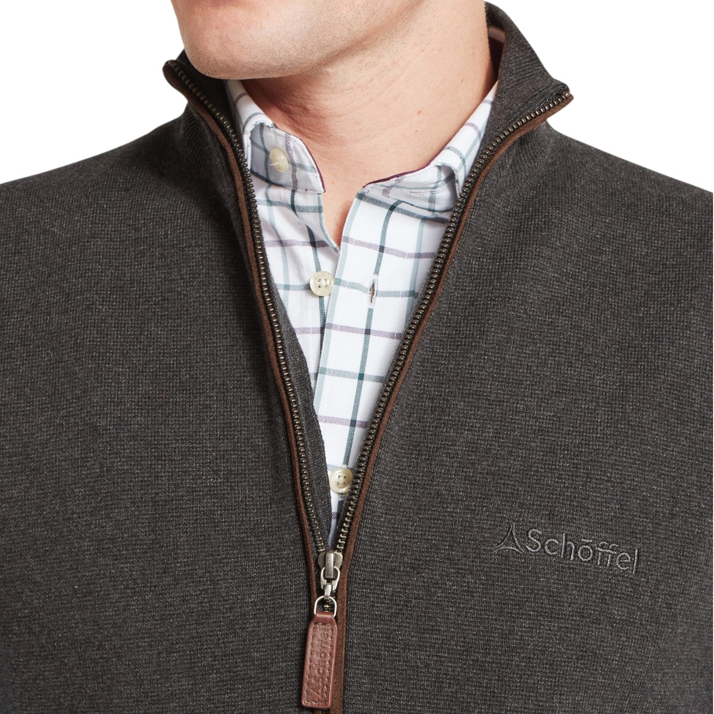 Close-up of a person wearing a brown jacket with a visible brand logo, over a plaid shirt.