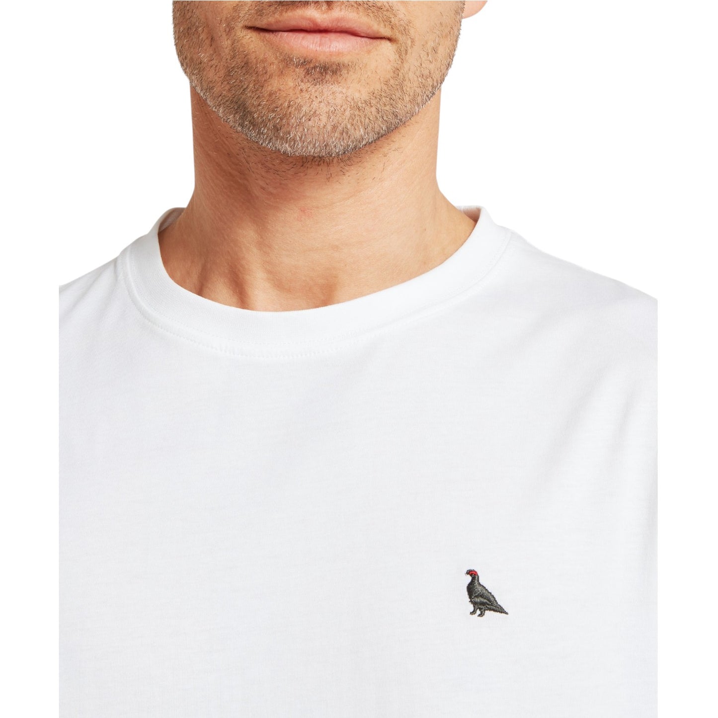 White t-shirt with a small bird emblem worn by a person on a white background
