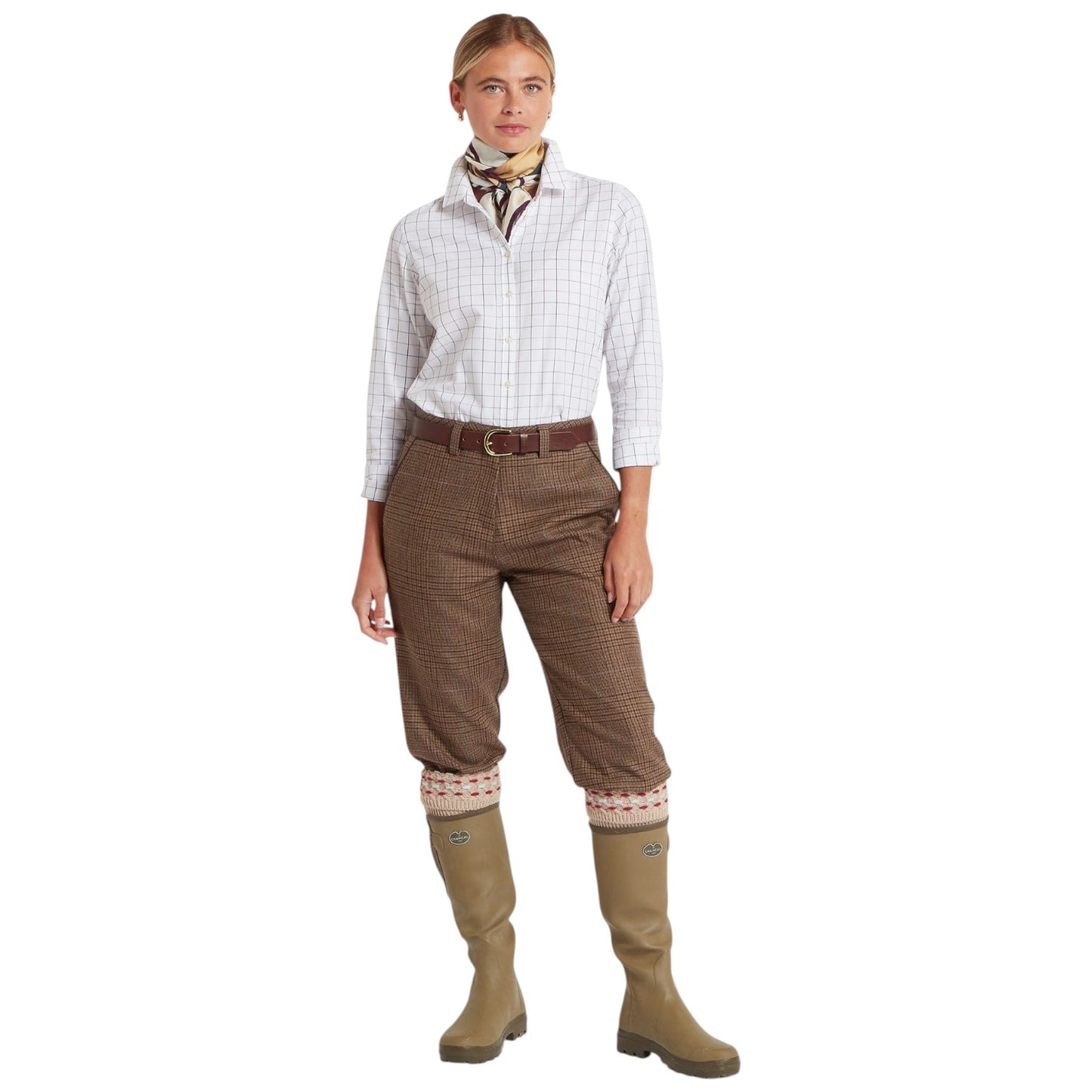 Woman wearing a checkered shirt, brown tweed pants, and green boots on a white background