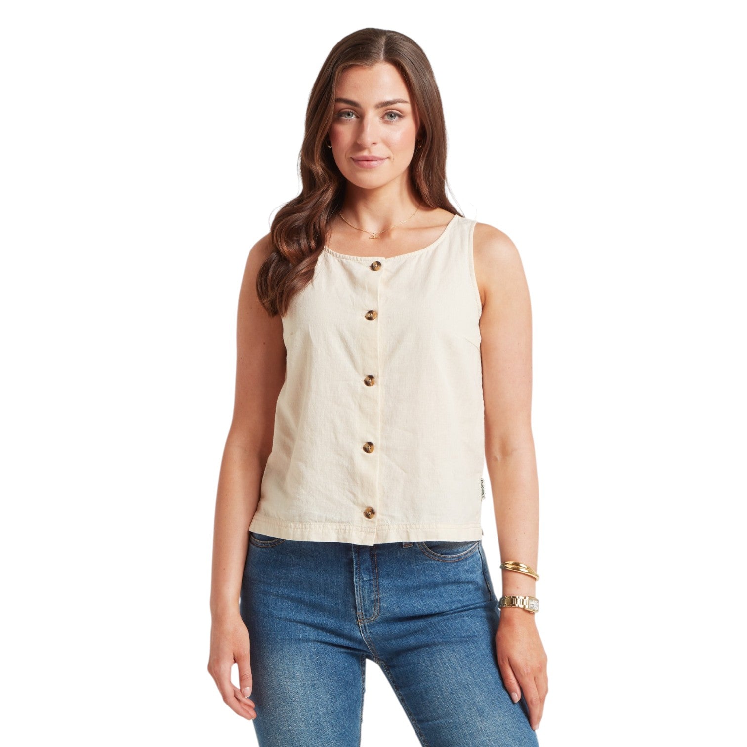 Woman wearing a beige sleeveless top with buttons and blue jeans on a white background