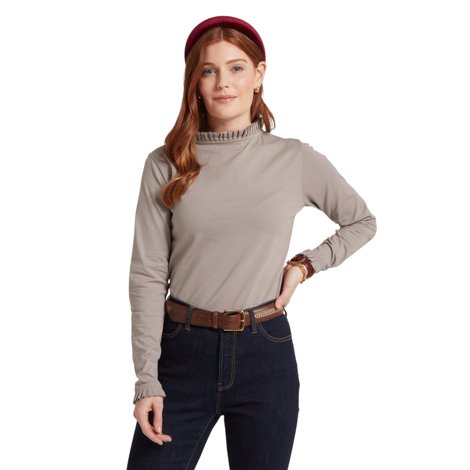 Woman wearing a beige turtleneck, dark jeans, and a red cap on a white background