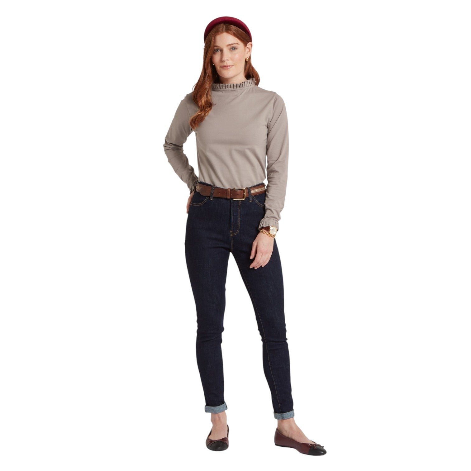 Woman wearing a beige long-sleeve top and dark jeans on a white background