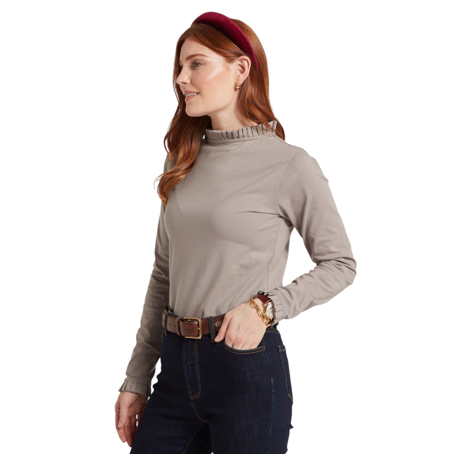 Woman wearing a beige long-sleeve top and dark jeans on a white background