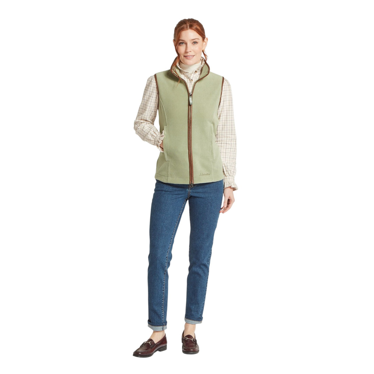 Woman wearing a green vest over a plaid shirt with blue jeans on a white background