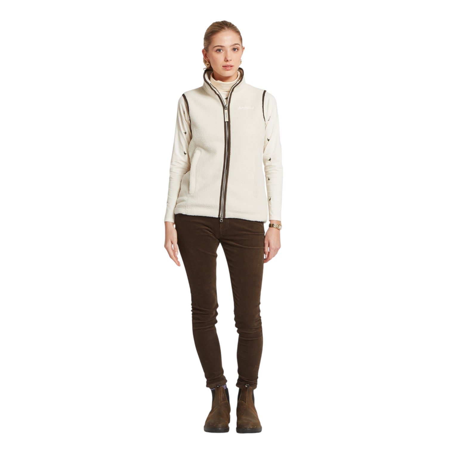 Woman wearing a cream-colored vest over a dark top and brown pants on a white background