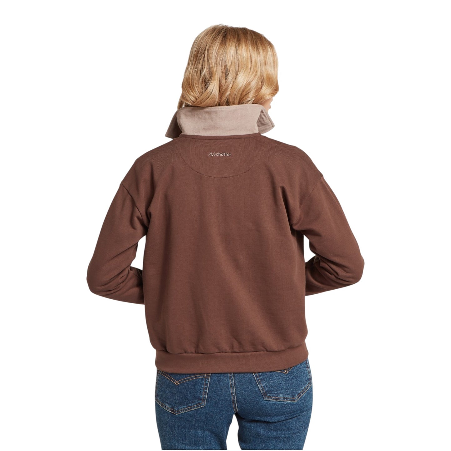 Person wearing a brown jacket with a visible brand logo on the back, standing against a white background.
