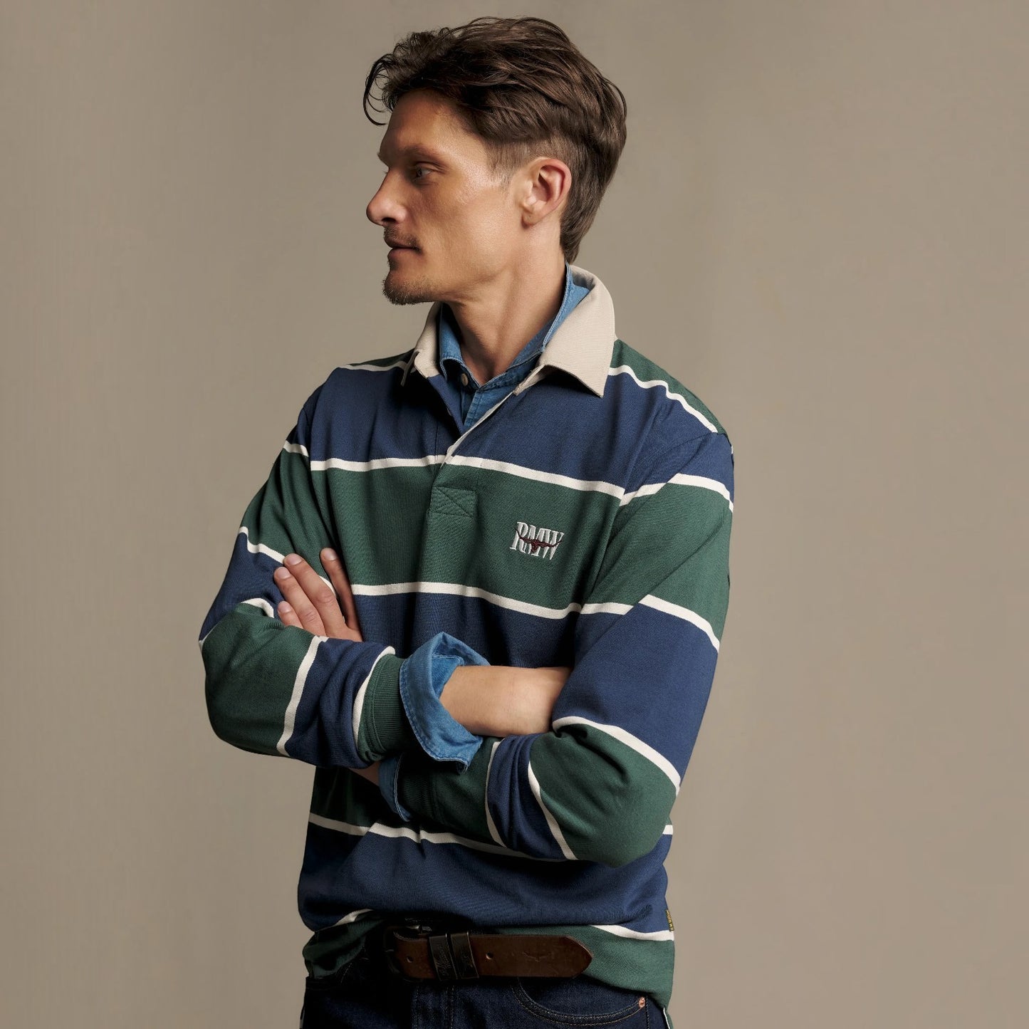 A man wearing a navy, green, and white striped rugby shirt with a cream collar, posed against a solid beige background.