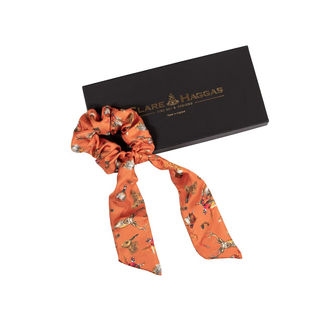 Orange patterned hair scrunchie with a black box featuring 'Clare Haggas' branding on a white background.