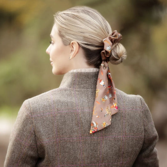 Woman with a floral hair tie in her bun, wearing a brown coat outdoors.