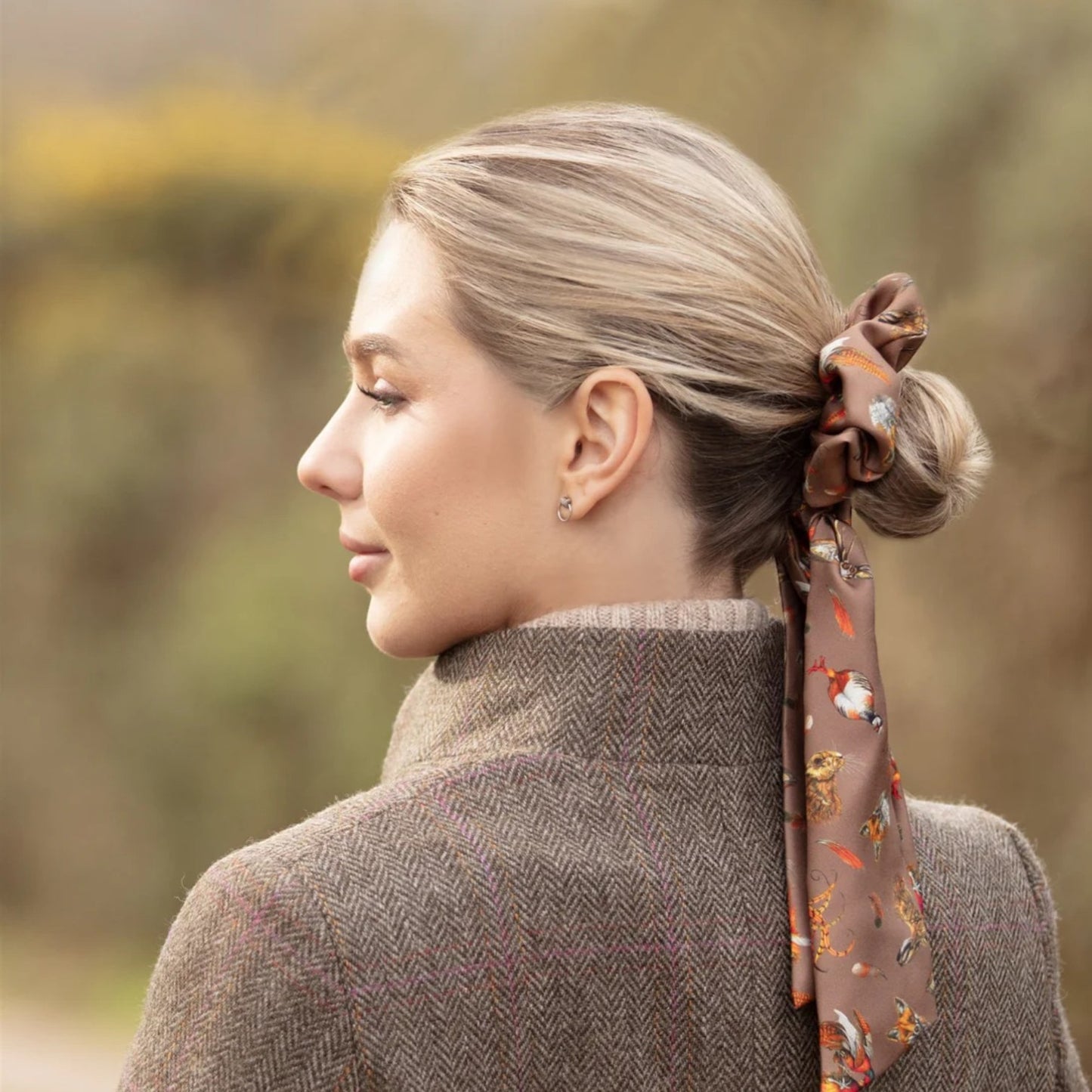 Woman with a patterned hair tie in her hair, wearing a coat outdoors.